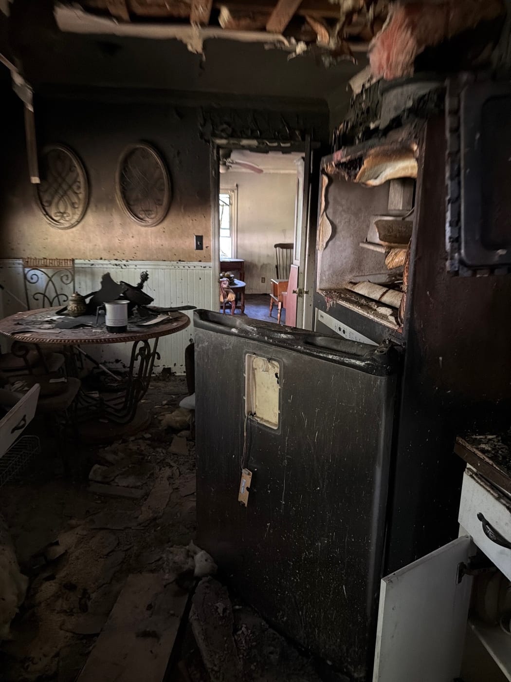 A fire-damaged kitchen with charred cabinets and soot across the walls and ceiling