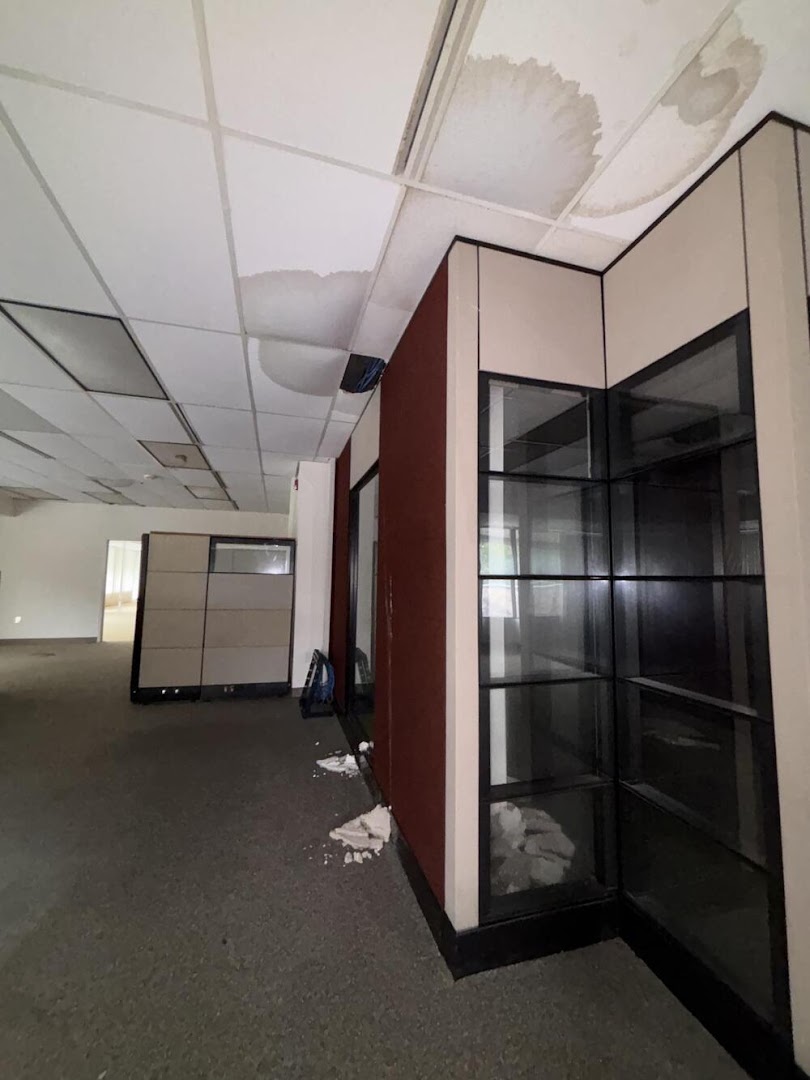 A commercial interior stripped back mid-repair, the ceiling grid emptied of its tiles and debris across the floor beside a display unit