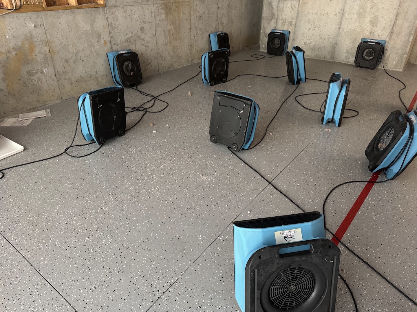 Eight air movers arranged around the perimeter of a stripped room, drying the structure