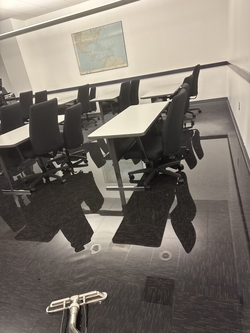 A commercial meeting room with the chairs stacked to one side and an extraction wand left on the wet carpet
