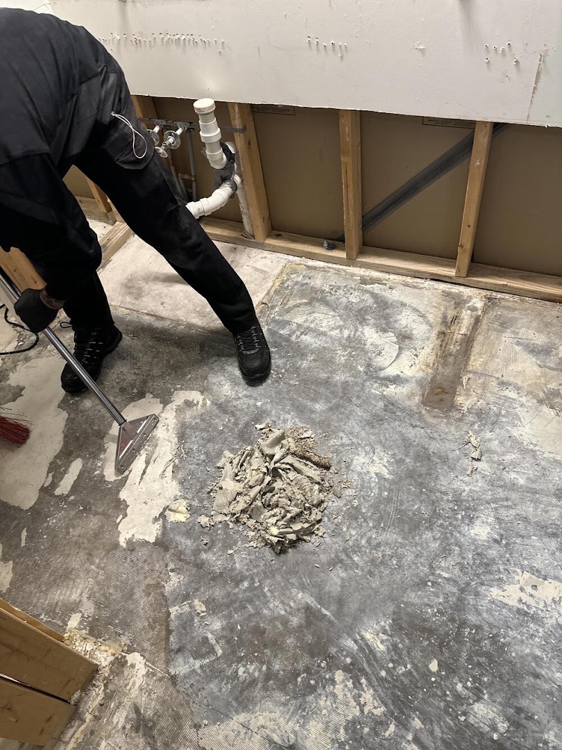 An AquaDry technician working an extraction wand across a stripped concrete floor, the wall behind opened back to the studs