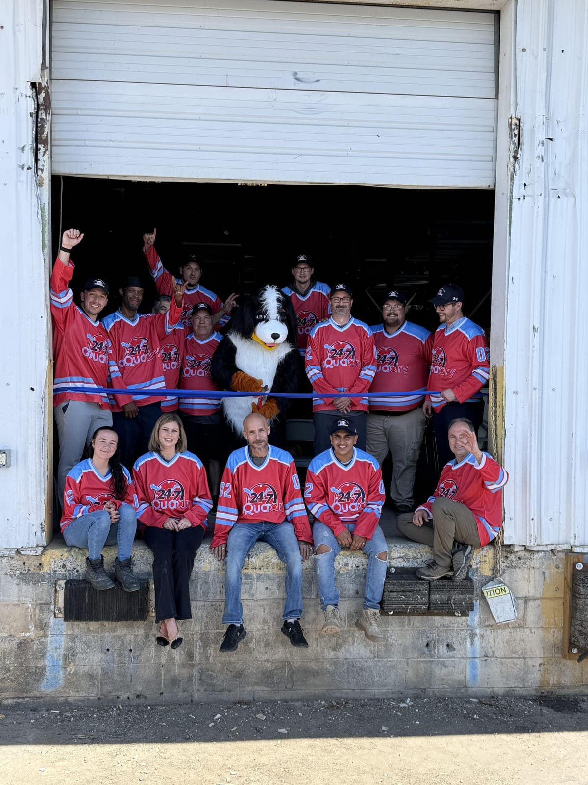 The 24-7 AquaDry team in team jerseys with the dog mascot at the shop's loading dock