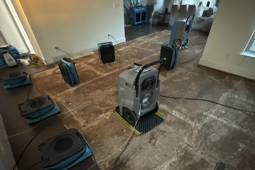 A stripped floor with eight air movers arranged around it and a dehumidifier running in the middle of the room