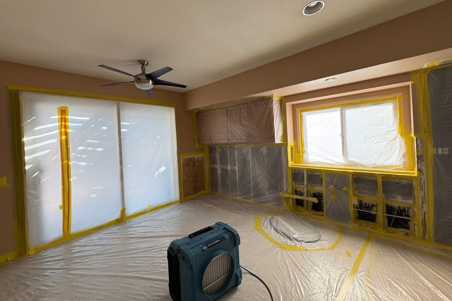 A room sealed in containment plastic with drywall cut open for inspection and an air scrubber running