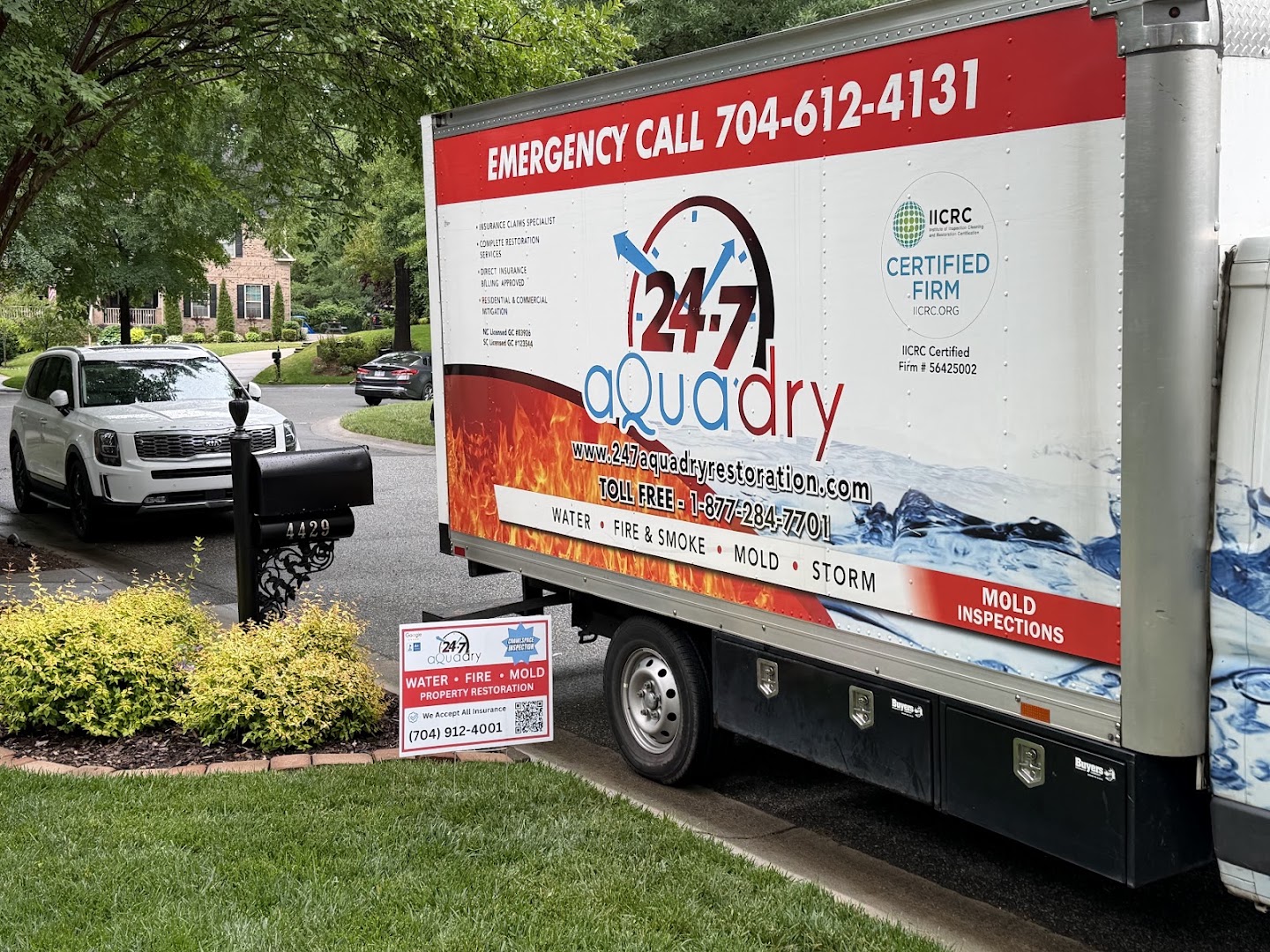 A 24-7 AquaDry box truck parked on a residential driveway with a company yard sign at the kerb